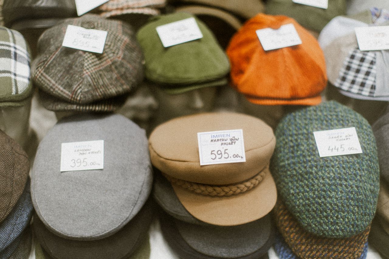 Vintage flat caps and newsboy hats displayed with price tags, showcasing variety in style and color.