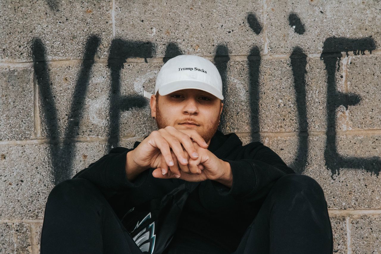 Adult male in front of graffiti wall wearing a cap with political statement. Urban and edgy portrait style.